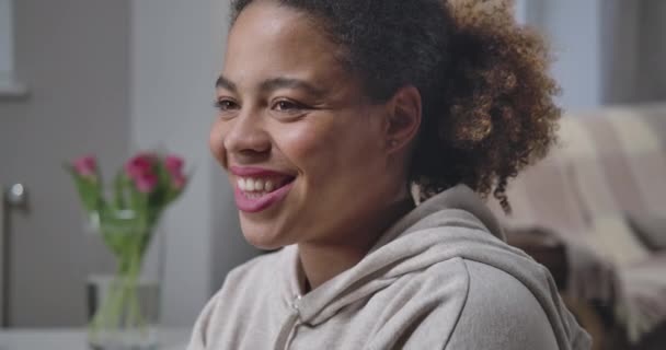 Foto de la feliz sonrisa de la joven afroamericana mirando hacia otro lado sonriendo en el interior. Primer plano retrato de alegre y relajada hermosa dama con sonrisa dentada en casa. Sede del cine 4k ProRes. — Vídeos de Stock