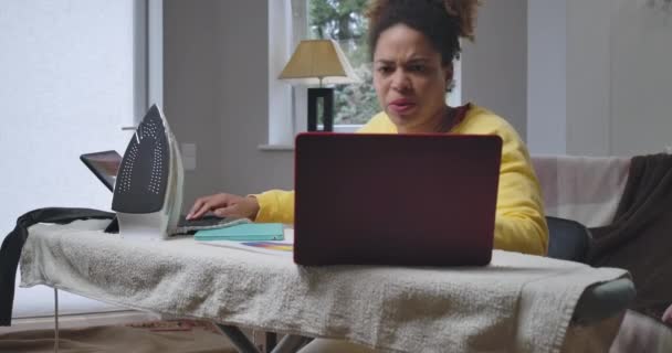 Απασχολημένος βιαστικά Αφρο-Αμερικανός γυναίκα μηνυμάτων σε απευθείας σύνδεση σε φορητό υπολογιστή και tablet με τόνισε την έκφραση του προσώπου. Νεαρός ανήσυχος εργαζόμενος στο γραφείο στο σπίτι για πανδημία. Κινηματογράφος 4k ProRes HQ. — Αρχείο Βίντεο