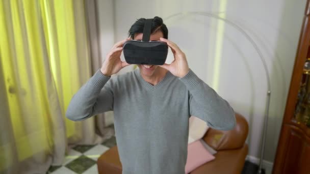 VR kulaklıklı mutlu Orta Doğulu adam evde oturma odasında duruyor. Heyecanlı, neşeli, yakışıklı adamın portresi. Kapalı alanlarda geziyor.. — Stok video