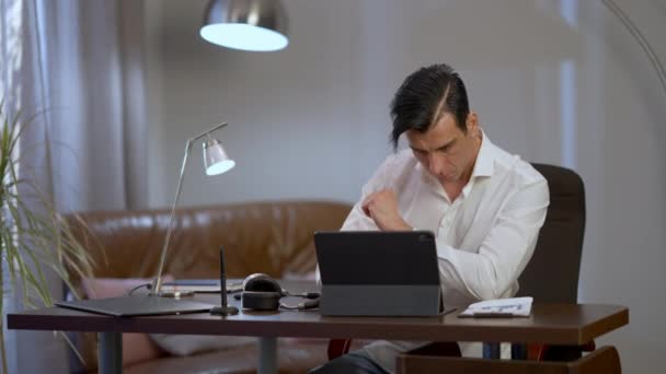 Konsantre Ortadoğulu adam merkez ofiste oturuyor ve akşamları internette çalışıyor. Ciddi bir şekilde odaklanmış yakışıklı iş adamı, salgının kilitlenmesi üzerine piyasayı analiz ediyor.. — Stok video