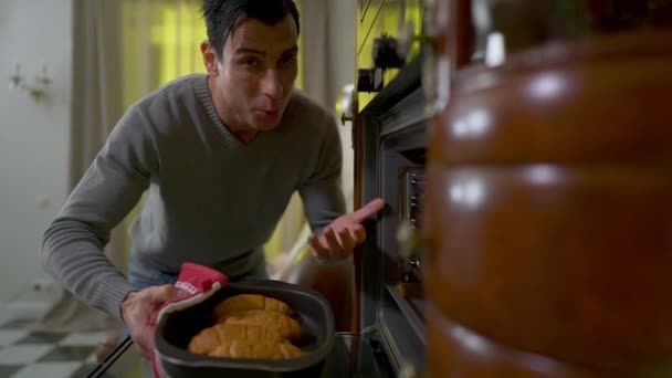 Boldog fiatal közel-keleti szakács kezében frissen sült croissant sütőlapon mutatja hüvelykujját felfelé a kamerába. Portré mosolygós magabiztos szakács otthon a konyhában. — Stock videók