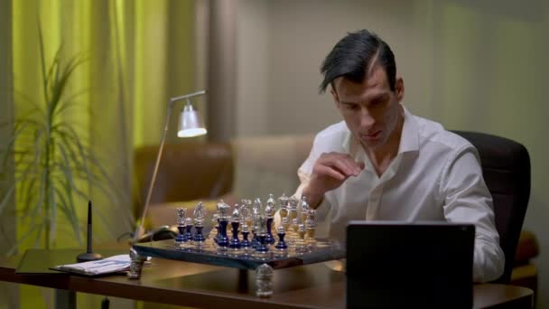 Художній молодий чоловік з Близького Сходу грає в шахи вдома, перевіряючи онлайн-відео. Портрет вправного серйозного гравця, який вдосконалює свій талант у приміщенні.. — стокове відео