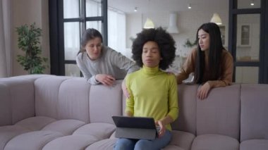 Uzak mesafeden oda arkadaşının dikkatini dağıtan Asyalı ve Kafkas kadınlarının geniş açılı görüntüsü. Gülümseyen Afrikalı Amerikalı serbest yazar işten tabletle çıkıyor ve arkadaşlarıyla ayrılıyor. Merkez ofis kavramı.