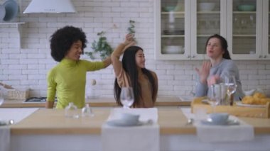 Üç kaygısız neşeli çokuluslu kadın mutfakta dans ederken eğleniyor. Mutlu pozitif, neşeli bayan arkadaşlar hafta sonu evde buluşmanın keyfini çıkarıyorlar. Boş zaman ve arkadaşlık kavramı.