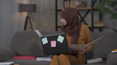 Aşırı yüklenmiş Ortadoğulu bir kadın, ofisteki belgeleri analiz ediyor. Tatmin olmamış yüz ifadesiyle koltuğa yaslanıyor. Aşırı çalışma ve tükenme kavramı.