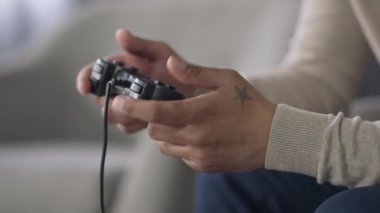 Yandan çekilmiş Afro-Amerikan ellerinin oyun kontrol tuşlarına bastığı yakın plan görüntüler. Evde video oyunu oynayan tanınmayan genç erkek oyuncu var. Boş zaman ve yaşam tarzı.