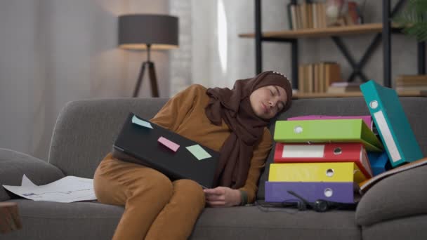 Ung smuk udmattet mellemøstlig kvinde sover på sofaen i hjemmekontoret med laptop og dokumenter. Portræt af træt overvældet attraktiv dame falder i søvn overarbejde. Træthedsbegrebet. – Stock-video