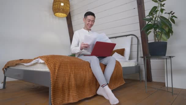 Jeune homme asiatique excité vomissant des graphiques faisant geste de victoire se réjouissant du succès de la stratégie d'entreprise assis sur le lit dans le bureau à domicile. Portrait de heureux gérant chinois joyeux avec sourire de dents à l'intérieur. — Video