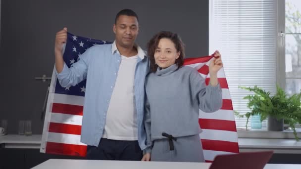 Porträtt av lyckliga rasblandat par poserar med USA flagga i köket hemma. Glad leende afroamerikansk man och vit kvinna tittar på kameran insvept i nationell symbol. Stolthet koncept. — Stockvideo
