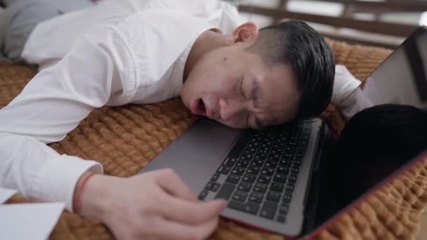 Joven chino cansado bostezando tumbado en el teclado de la computadora portátil siesta en la oficina en casa. Un asiático agotado con exceso de trabajo que duerme en la cama descansando en el trabajo remoto. Cansancio y agotamiento. — Vídeo de stock