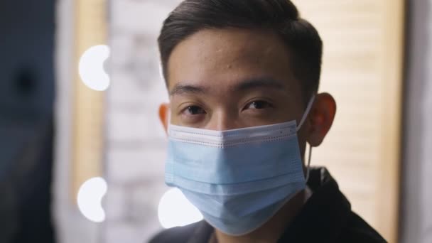 Headshot de jeune homme chinois en masque facial Covid regardant la caméra avec une expression faciale sérieuse. Gros plan portrait d'un beau asiatique posant à l'intérieur sur une pandémie de coronavirus. Nouveau concept normal. — Video