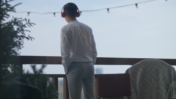 Back view of confident Asian man in headphones looking away from deck closing laptop and leaving in slow motion. Successful young positive Chinese manager on remote working in home office. — 비디오