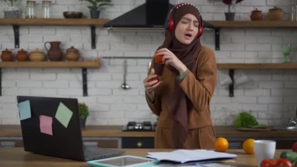 Veselá mladá krásná žena v hidžábu a sluchátka zpívající tanec vaření zdravý veganský salát v kuchyni. Portrét radostné bezstarostné dámě ze Středního východu, která se baví držením zeleniny v rukou. — Stock video