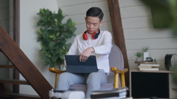 Jeune homme asiatique debout depuis un fauteuil confortable et laissant passer la caméra. Gestionnaire professionnel chinois sérieux dans le salon de bureau à domicile à l'intérieur avec tablette. Mouvement lent. — Video