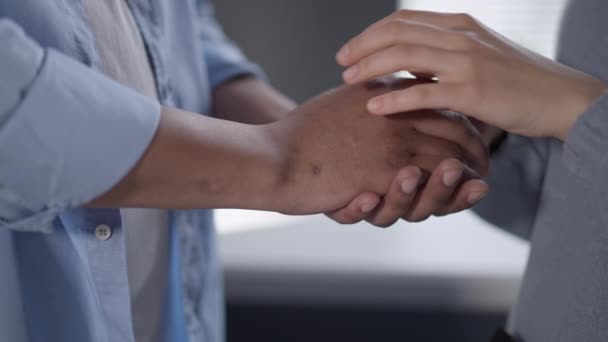 Close-up of unrecognizable interracial couple holding hands indoors. Young Caucasian woman and African American man stroking palms. Love and unity concept. — Stock Video