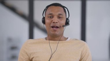 Web kamerasında gülümseyen Afrikalı Amerikalı genç adamın yavaş çekimde el sallayıp konuşmasının görüntüsü var. Sanal konferansta iş konuşmasında kendinden emin çalışanları karşılayan portre.