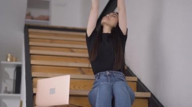 Genç, çok çalışan Asyalı kadın merdivenlerde ofis odasında esneme hareketleri yapıyor. İçerde çalışan başarılı, güzel, ince iş kadını portresi. Yeni normal yaşam tarzı.