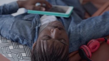 Göğsünde tablet tutarak uyuyan yorgun Afrikalı Amerikalı bir adamın portresi. İş yerinde rahat bir ofiste kestirirken yorgun ve yakışıklı bir adamın yakın çekimi. İş ve dinlenme.