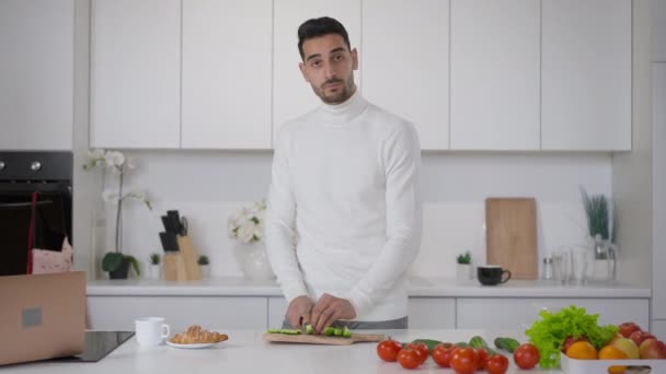 Blog de comida saudável do jovem homem do Oriente Médio cozinhar salada vegan saudável na cozinha. Web câmera POV de confiante bonito jovem chef cortar legumes falando e gesticulando. — Vídeo de Stock