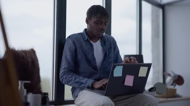 Overworked man sending e-mail sighing closing laptop and leaving. Tired young African American manager messaging online from home office working on windowsill. New normal lifestyle. — Stock Video