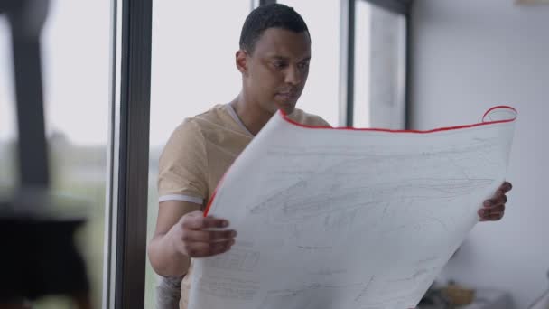 Retrato de um talentoso arquitecto afro-americano a analisar o projecto no escritório em pé à janela. Jovem concentrado ocupado olhando para o pensamento do plano arquitetônico. Conceito de talento. — Vídeo de Stock