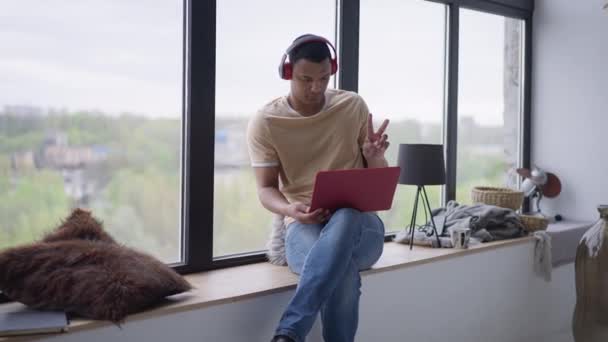 Vooraanzicht portret van serieuze gefocuste jonge man in hoofdtelefoon zwaaiend hallo op video chat op laptop praten. Zelfverzekerde Afro-Amerikaanse manager conferencing in het thuiskantoor binnen. — Stockvideo