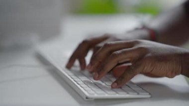 Kapalı mekanda bilgisayar klavyesine yazı yazan Afrikalı Amerikalı erkeklerin yakın çekimi. Ofiste çalışan tanınmayan genç bir adam e-posta yolluyor. Uzak çalışma ve iş.