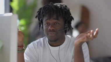 Kulaklıklı ciddi bir adamın arka planda aynaya bakan bulanık bir kadınla konuştuğu bir web kamerası görüntüsü. Afro-Amerikan iş danışmanının portresi..