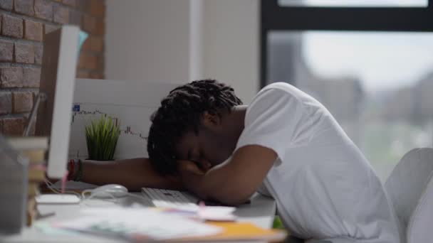 Ung utmattad man ligger på bordet och sover på hemmakontoret. Trött överbelastad afroamerikansk professionell tupplur inomhus. Överarbetning och utbrändhet. — Stockvideo
