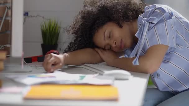 Jovem afro-americana impressionada dormindo na mesa em casa no dia ensolarado. Cansado exausto belo freelancer magro com olhos fechados dentro de casa no tempo de trabalho. Burnout e excesso de trabalho. — Vídeo de Stock