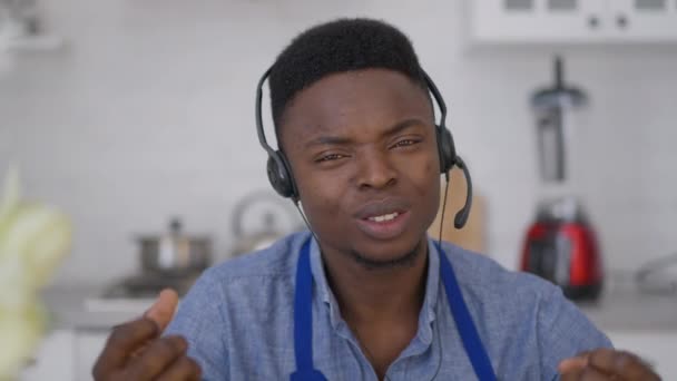 Close-up portret van drukke Afro-Amerikaanse jongeman in oortelefoons die in slow motion praat en naar de camera kijkt. Video chat POV van zelfverzekerde business consultant bespreken strategie winstgevendheid online. — Stockvideo