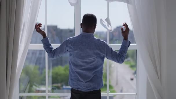 ストレスの多いアフリカ系アメリカ人男性のバックビューは、自宅のオフィスで窓の外を見て書類検査をスローします。コロナウイルス危機の絶望的な若いビジネスマンを屋内で負担. — ストック動画