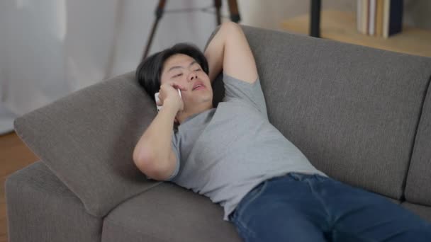 Portret pewnego siebie mężczyzny, leżącego na kanapie i rozmawiającego przez telefon. Skoncentrowany azjatycki ekspert omawiający strategię biznesową z komfortowego salonu biurowego. Praca na odległość. — Wideo stockowe