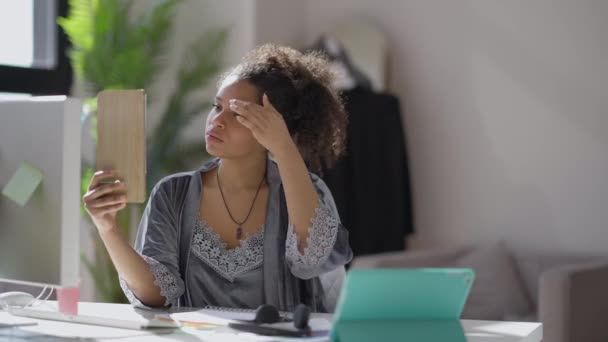 Junge Afroamerikanerin sieht morgens im Spiegel, wie ein Mann im Hintergrund auf einem Sessel sitzt. Porträt eines charmanten, wunderschönen Managers, der sich auf eine virtuelle Konferenz vorbereitet. — Stockvideo