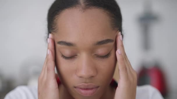 Egy közeli kép a kimerült, túlterhelt afro-amerikai fiatal nőről migrénes masszírozó halántékkal a kamerába nézve. Fejlövés fáradt gyönyörű vékony hölgy szenved fejfájás otthon iroda. — Stock videók