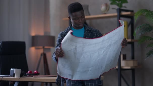 Mellombilde av talentfull afrikansk-amerikansk kreativ mann som analyserer planleggingsplanlegging. Portrett av faglært ung landskapsarkitekt i pyjamas som står på hjemmekontor. – stockvideo