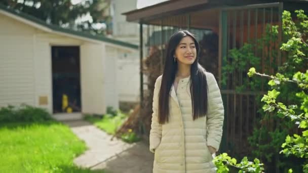 Mladá sebevědomá Asiatka kráčející v letní jarní zahradě a obdivující keře a kvetoucí stromy na slunci. Portrét hrdé zahradnice, která se venku usmívá. — Stock video