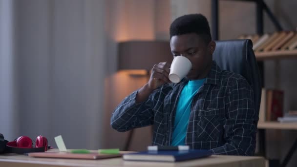 Oturma odasında çay ya da kahve içen yakışıklı Afrikalı Amerikalı adamın portresi. Bin yıllık başarılı girişimci pijamalarıyla akşam ya da sabah iş yerinde.. — Stok video