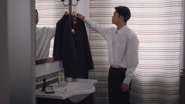 Junger asiatischer Mann im Hochzeitsblazer auf Kleiderbügel, der vom Badezimmer weggeht. Porträt eines ernsthaften selbstbewussten eleganten Bräutigams, der sich am Hochzeitsmorgen zu Hause vorbereitet. Kerl geht. — Stockvideo