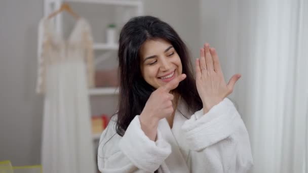 Joyeux jeune femme avec le sourire de dent pointant vers la bague de fiançailles sur la main gauche souriant en regardant la caméra. Portrait de mariée excitée du Moyen-Orient vantant des bijoux le matin du mariage à l'intérieur. — Video