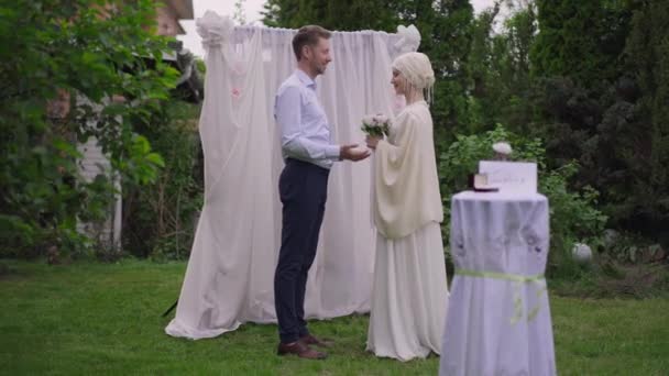 Amplio plano de novia y novio felices y amorosos de pie en el altar al aire libre tomados de la mano hablando. Oriente Medio joven mujer y hombre caucásico disfrutando de la mañana de bodas juntos, vinculación y el concepto de matrimonio — Vídeos de Stock