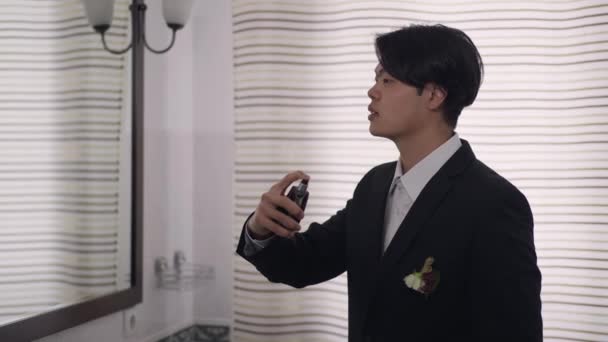 Side visning af ung asiatisk mand i bryllupsdragt sprøjtning parfume i slowmotion ildelugtende duft. Portræt af selvsikker glad brudgom bliver klar i badeværelset derhjemme. Elegance og ægteskab. – Stock-video
