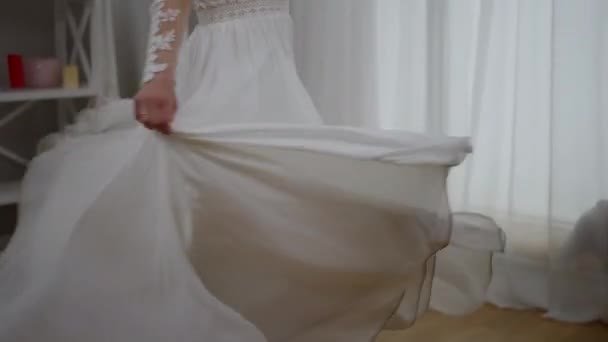 幸せな陽気な中東の花嫁はエレガントな白いウェディングドレスで笑って回転します。カメラは屋内で結婚式の準備を楽しんでスリム豪華な自信の女性として上に移動します. — ストック動画