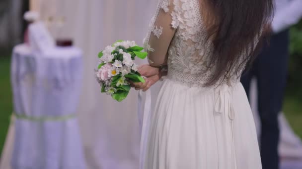 Vista posteriore di snella sposa mediorientale irriconoscibile in elegante abito bianco che tiene bouquet da sposa in piedi all'aperto. Giovane donna fiduciosa amorevole sposarsi. Romanticismo e amore. — Video Stock