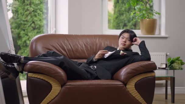 Plan large de marié asiatique heureux couché sur un fauteuil confortable à l'intérieur rêvant le jour du mariage. Portrait d'un bel homme confiant et réfléchi planifiant l'avenir dans un salon confortable à l'intérieur. — Video