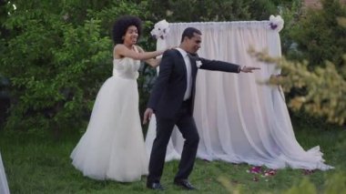 Neşe dolu Afrikalı Amerikalı yeni evlilerin düğün sunağındaki yaz bahçesinde yaptığı komik dans. Takım elbiseli neşeli gelin ve takım elbiseli damat açık havada evlilik töreninde eğleniyor..