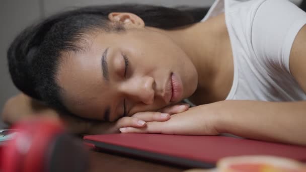 Faccia da primo piano di una giovane afroamericana affaticata che dorme sul tavolo in ufficio. Testa di stanca esausta donna freelance pisolino al chiuso durante l'orario di lavoro. Multitasking e stile di vita. — Video Stock