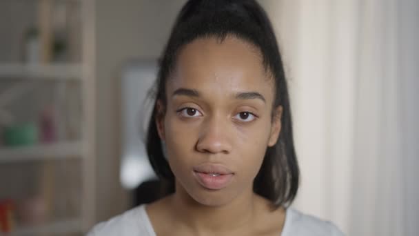 Närbild ansikte smal vacker afroamerikansk kvinna med bruna ögon tittar på kameran med allvarliga ansiktsuttryck. Huvudskott porträtt av självsäker ung tusenårig poserar inomhus. — Stockvideo