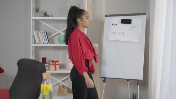 Vue de côté de mince afro-américaine jeune femme d'affaires debout dans le bureau à domicile au graphique d'affaires sur la pensée tableau blanc. Smart belle femme tenant verre d'eau citron planification stratégie de démarrage. — Video