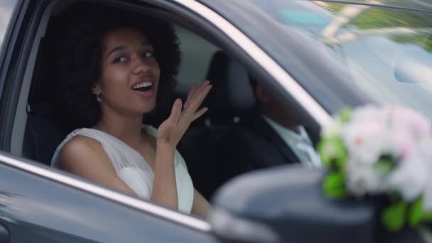 Elegante joven novia delgada en vestido de novia blanco sentado en el coche sonriendo. Retrato de feliz alegre mujer hermosa afroamericana casarse. Concepto de estilo de vida y felicidad. — Vídeos de Stock